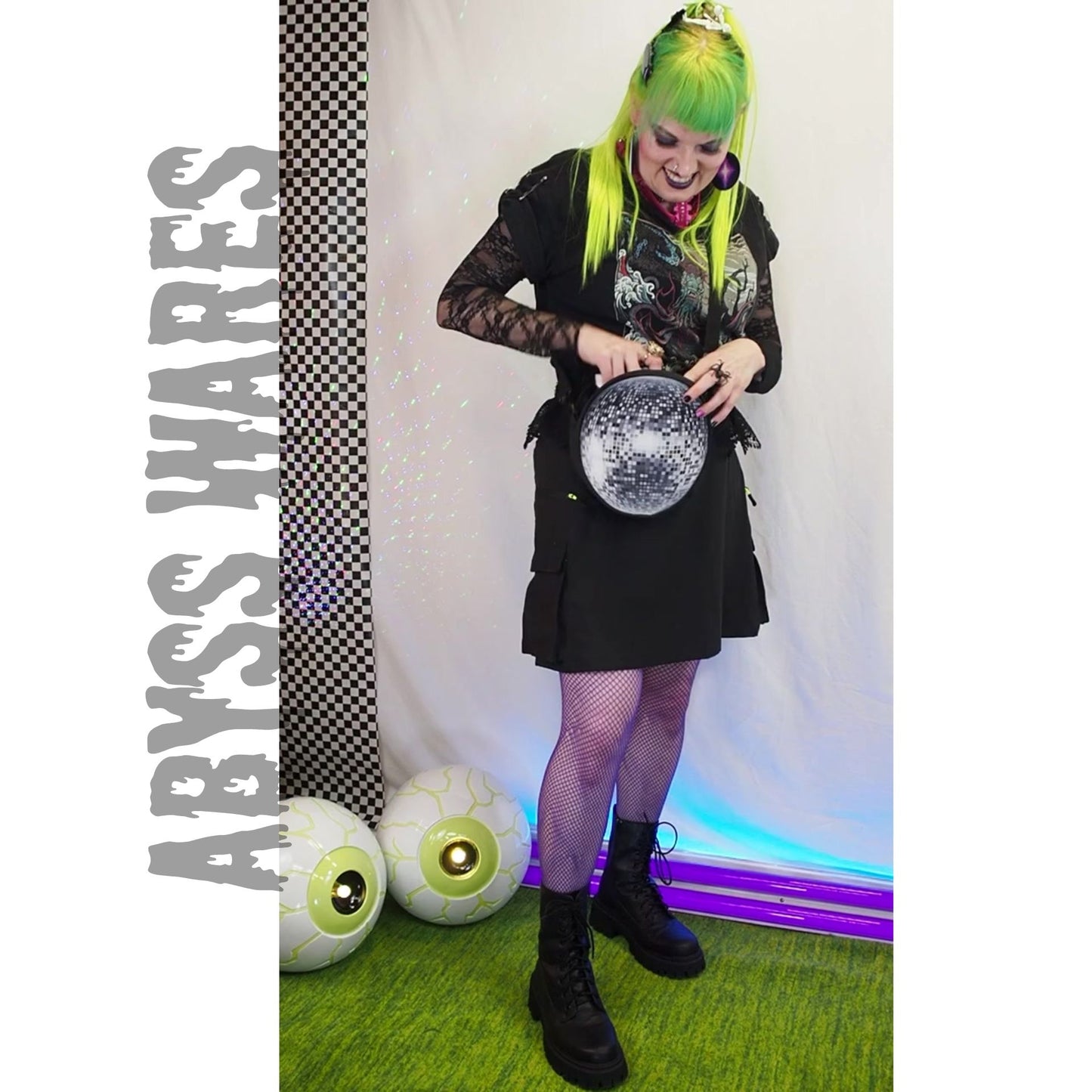 Person with neon green hair holding a disco ball print crossbody bag in front of a 'Abyss Wares' branded backdrop.