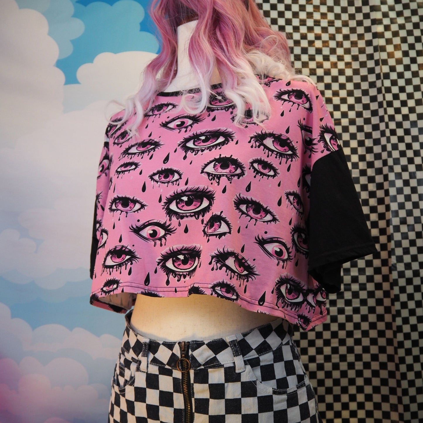 Person wearing a pink crop top with eye pattern and checkered skirt against a colorful background