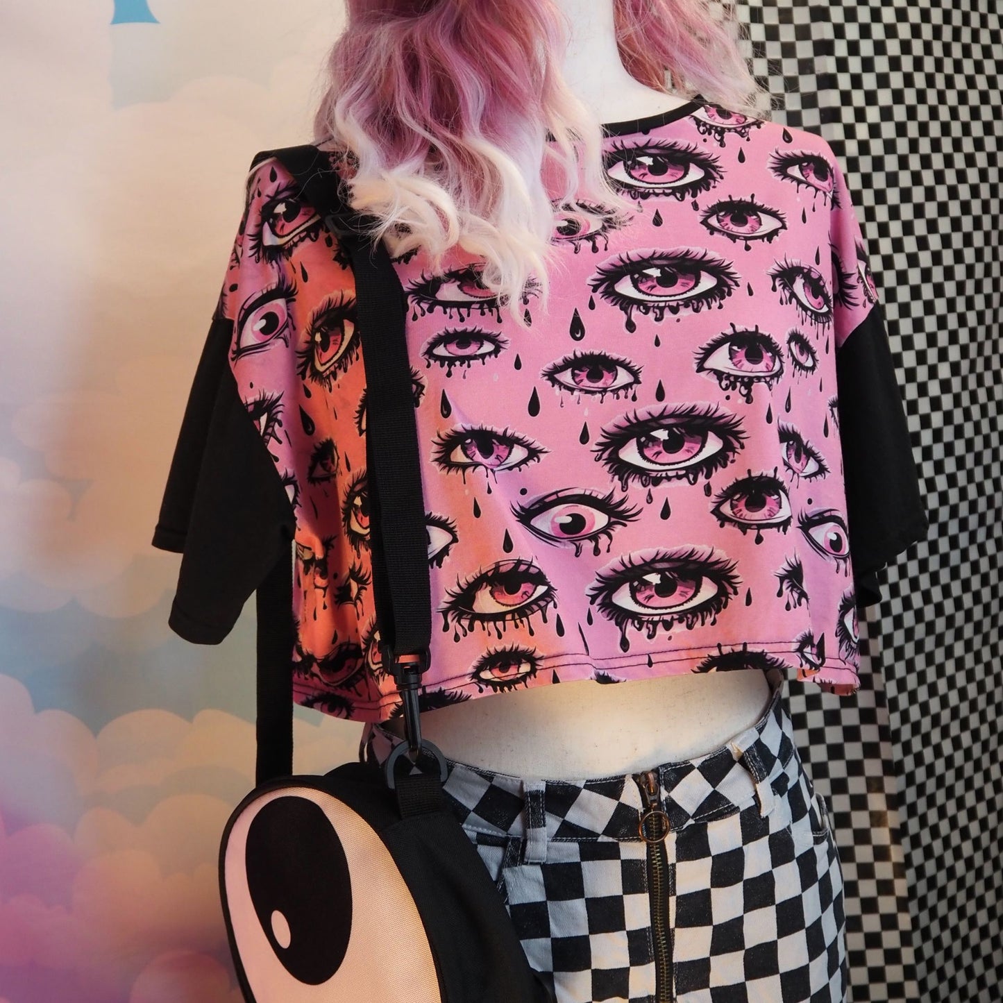 Person wearing a pink crop top with eye pattern and black pants against a colorful background