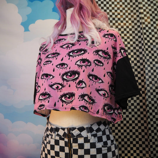Person wearing a pink crop top with eye pattern and checkered skirt against a colorful background