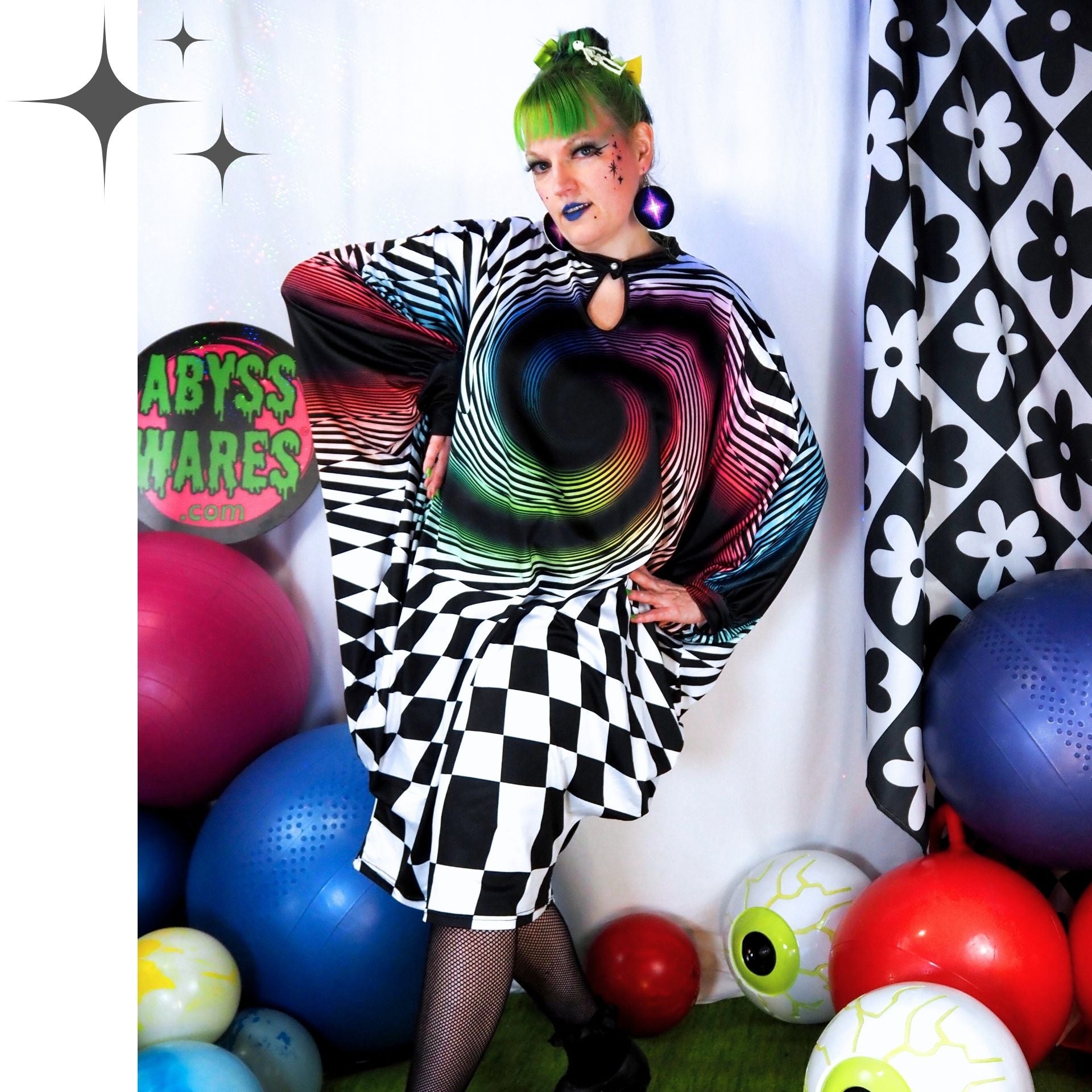 Person wearing a colorful, spiral-patterned dress with checkered skirt, surrounded by balloons and patterned curtains.