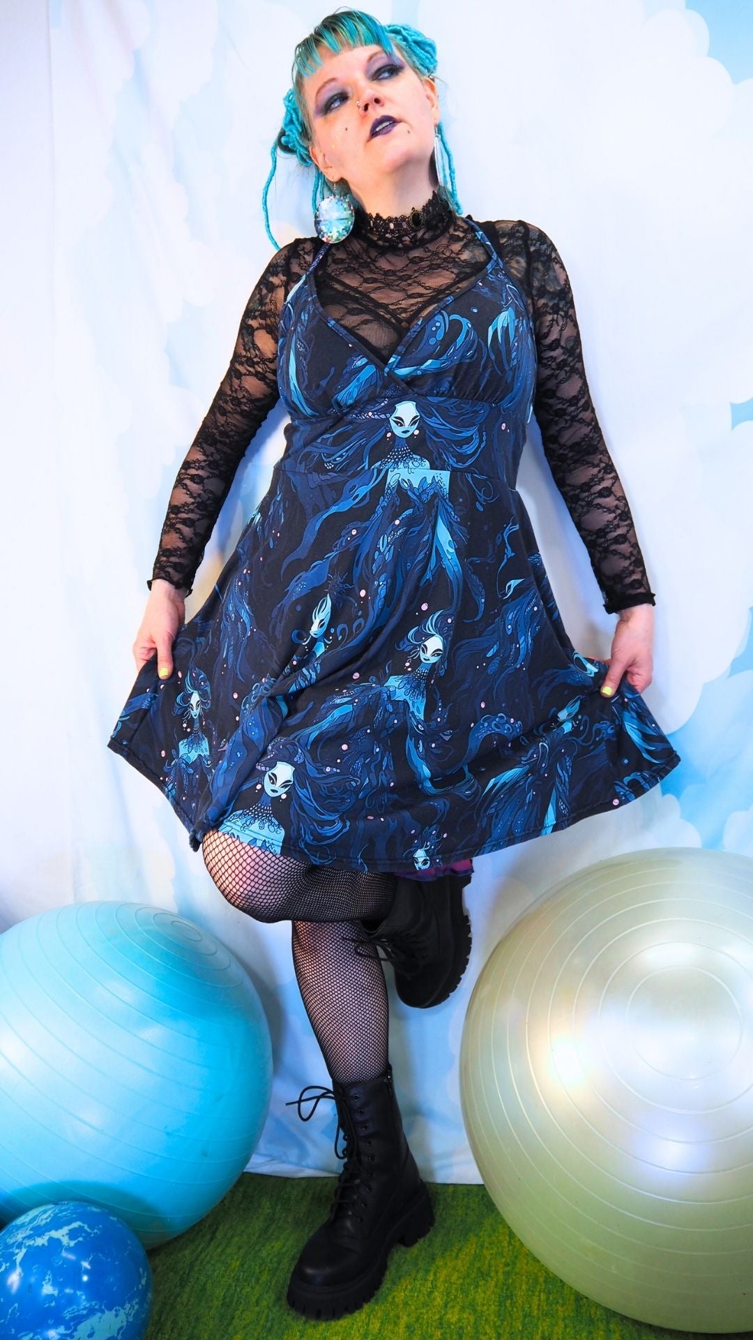 Person wearing a dark blue dress with a sea witch tentacle selkie pattern, standing next to balloons on a light background