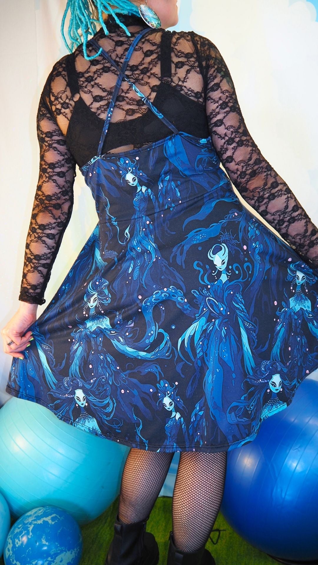 Person wearing a blue and black dress with a mermaid design, standing among blue balloons.