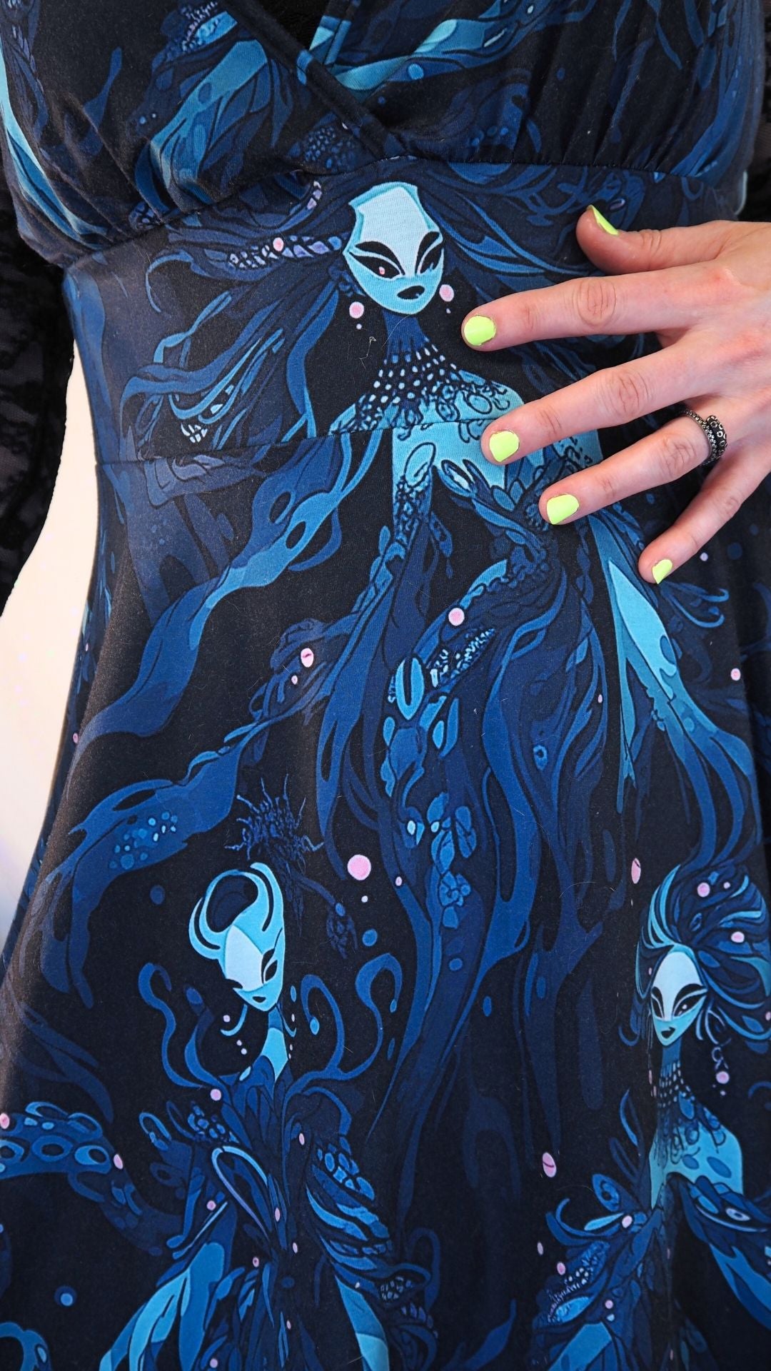 Close-up of a dark blue dress with mermaid pattern and hand holding it.