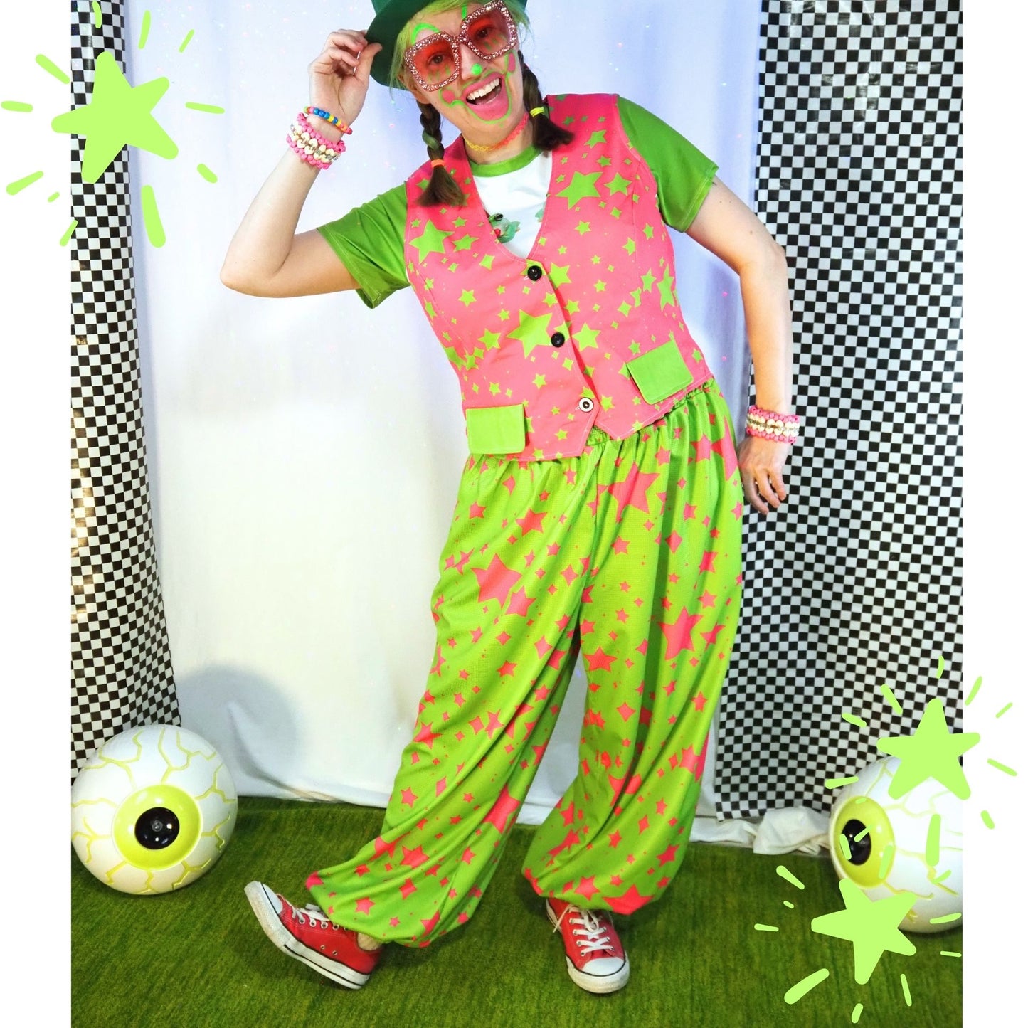 Person wearing a colorful outfit with pink vest and green pants, standing against a checkered curtain.